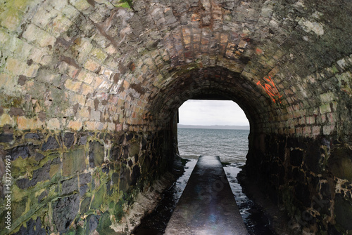 Dirty water runs down the sides of a path through a sewer tunnel to flow out to the sea.