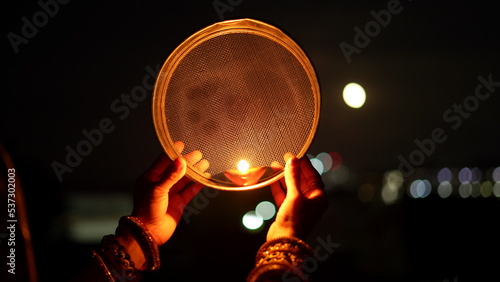 Woman hand holding Karwa Chauth strainer for the Karwa Chauth celebration on the night. Karwa Chauth strainer and Diya oil lamps for the Karwa Chauth celebration on the night © Govind
