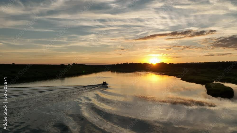 Aerial view. A small fishing boat with a motor floats on the calm water of the river at sunset. The setting sun and the sky are beautifully reflected in the river. Aerial view. A small fishing boat with a motor floats on the calm water of the river at sunset. The setting sun and the sky are beautifully reflected in the river.