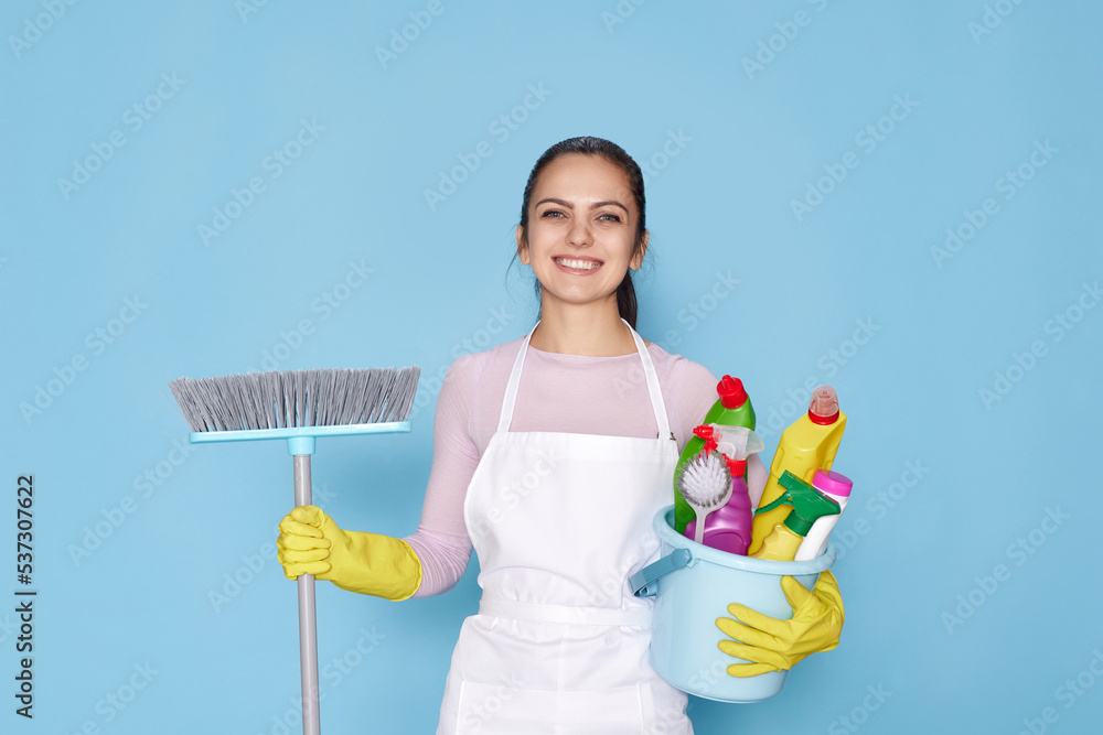 woman in gloves and cleaner apron holding bucket of detergents and broom woman in gloves and cleaner apron holding bucket of detergents and broom