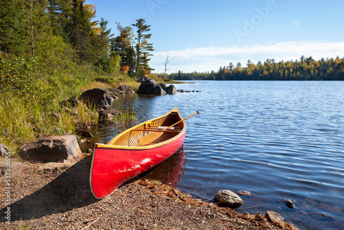 Red wooden canoe on shore of northern Minnesota lake with rocks and pines along the shore