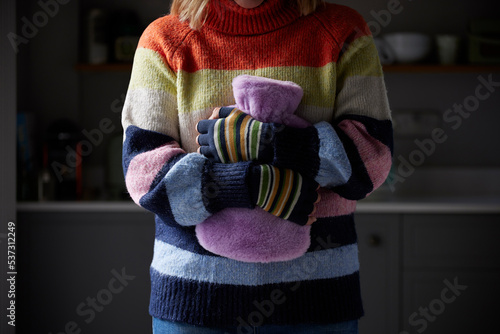 Woman In Gloves Hugging Hot Water Bottle Trying To Keep Warm During Cost Of Living Energy Crisis photo