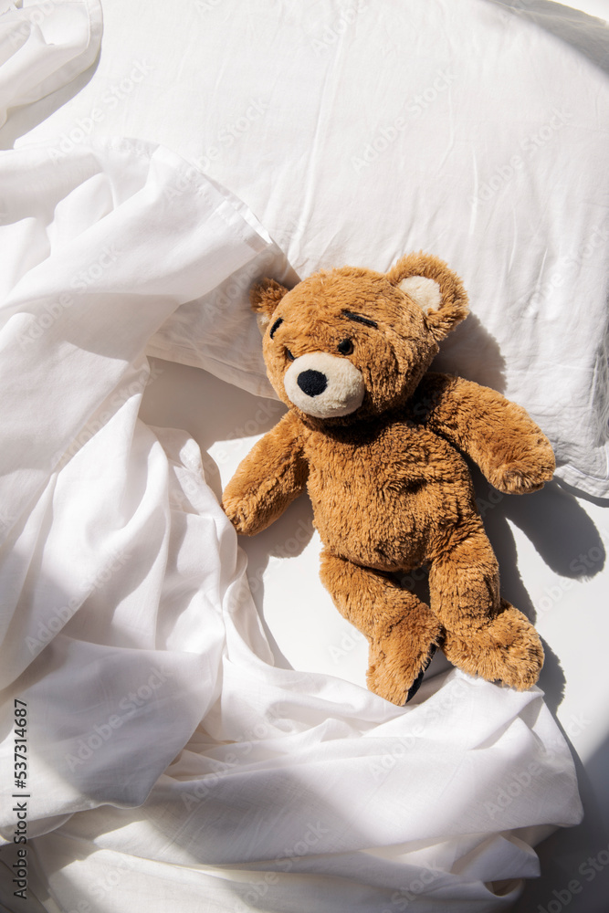 Soft toy bear lies on the bed under natural light. Top view, flat lay