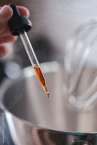 Pipette with vanilla extract close-up in hand with soft focus against the backdrop of a blurred kitchen. Cooking recipes. Ingredient for adding to confectionery, desserts, ice cream and other dishes