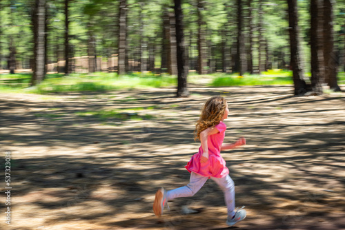 A girl running through the forest on a sunny day. © Juliana Swenson