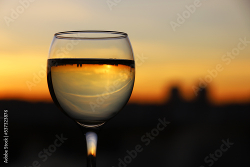 Glass with white wine on sunset sky and city background. Concept of celebration, wine industry