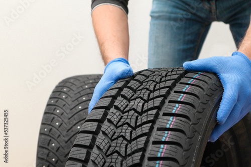 Replacement of winter and summer tires. Mechanic holding a tire at the white background. winter studded tyre, tires replacement © Trik