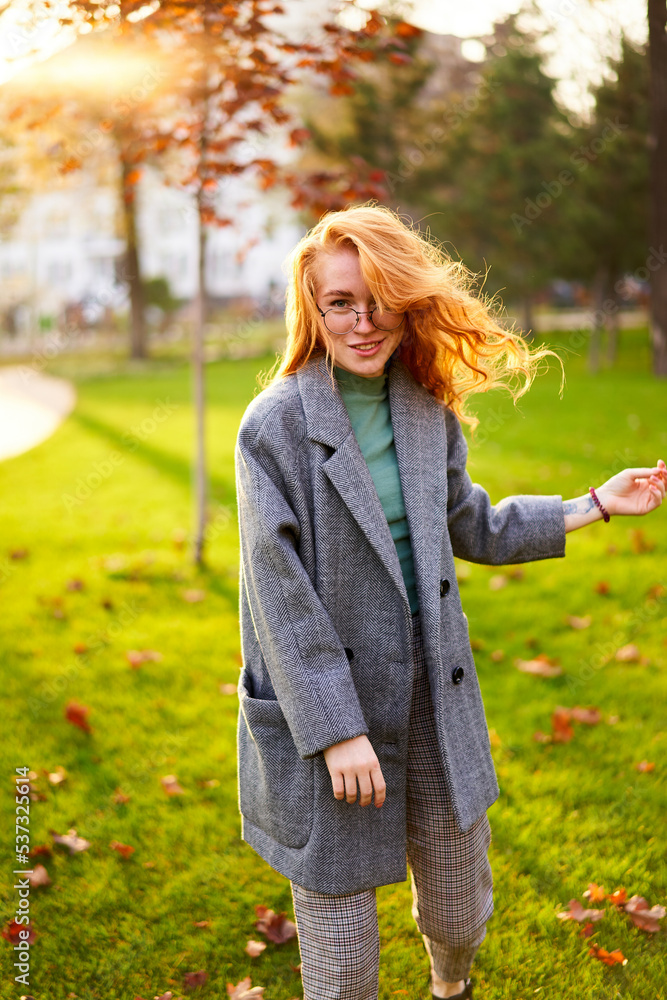 Redhead smiling pretty woman walking in park on sunny autumn day. Elegant female poses in stylish authentic outfit has fun laughing on green lawn with vivid foliage, leaves. Girl enjoys fall season. Redhead smiling pretty woman walking in park on sunny autumn day. Elegant female poses in stylish authentic outfit has fun laughing on green lawn with vivid foliage, leaves. Girl enjoys fall season.