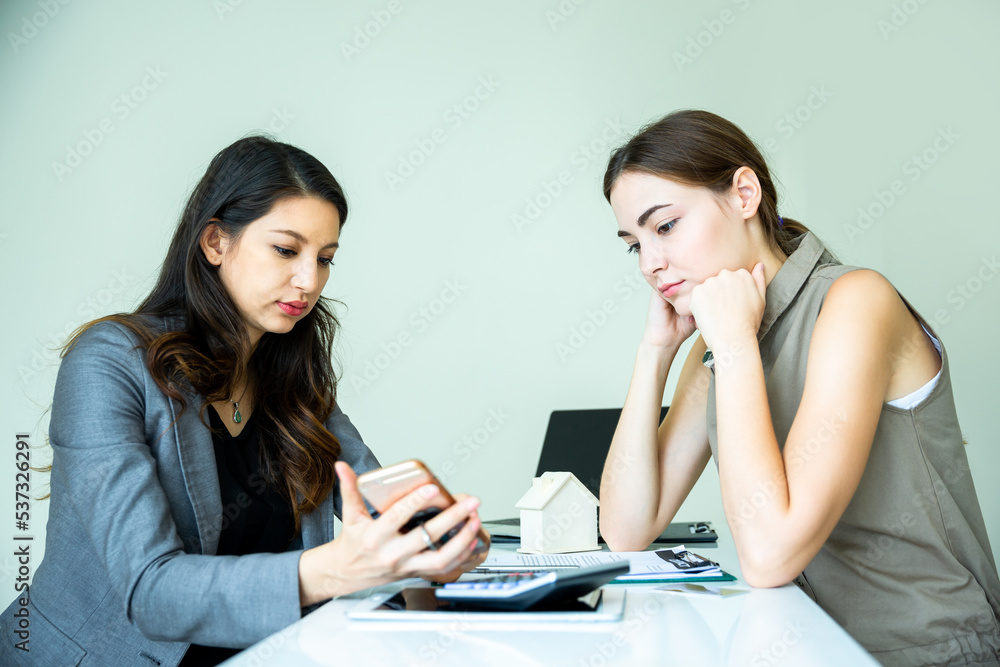 Two expertise business women in well dressed are checking the selling and interest about the property on internet by using electronic device in the office background. Business concept with copy space. Two expertise business women in well dressed are checking the selling and interest about the property on internet by using electronic device in the office background. Business concept with copy space.