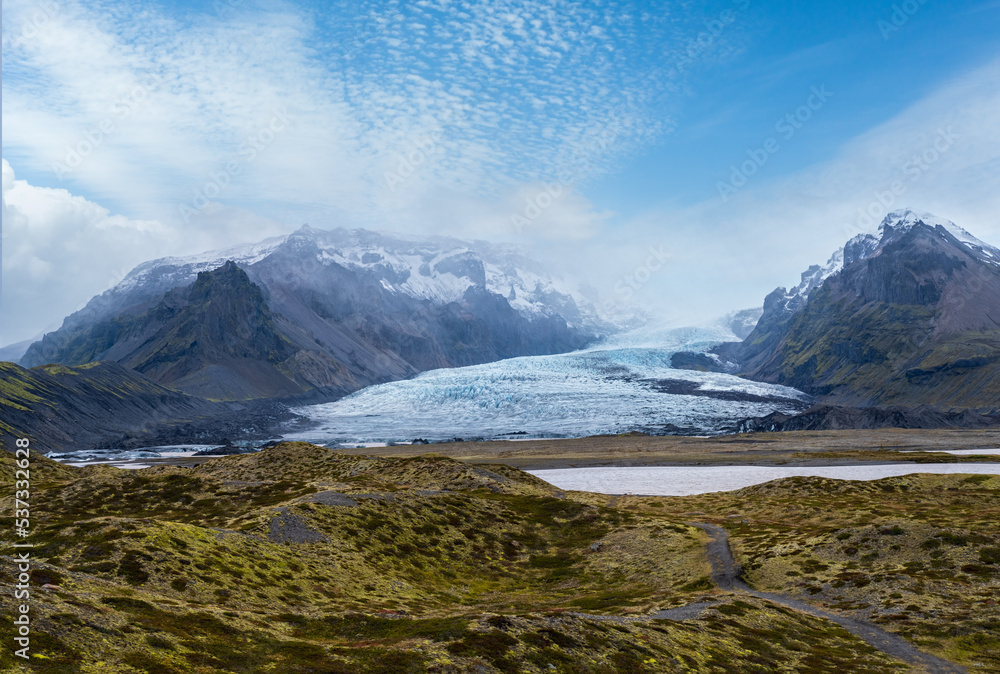 Glacier tongue slides from Vatnajökull icecap or Vatna Glacier near subglacial Öræfajökull volcano, Iceland. Glacial lagoon with ice blocks and surrounding mountains.