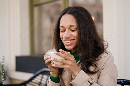 Fototapeta Naklejka Na Ścianę i Meble -  Young smiling african american girl drinking coffee in a cozy cafe. Holidays, lunch time and vacation concept      