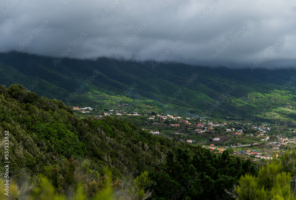 Village in the distance with incredible landscape of mountains full of green colour and a sky covered by clouds.