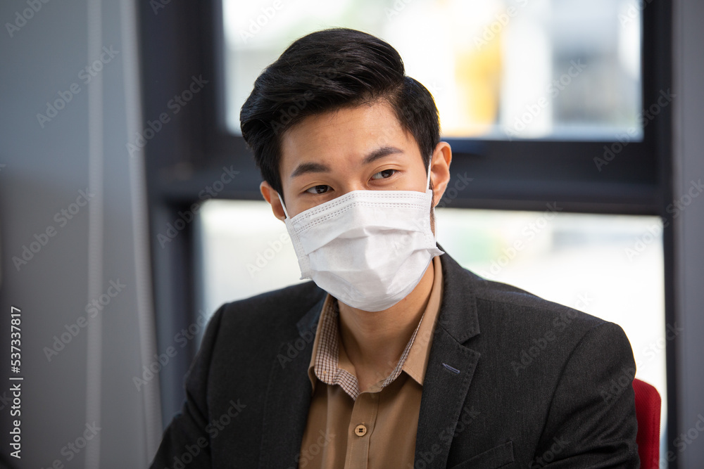 Asian male business employee wearing protective mask sitting at desk in the office Asian male business employee wearing protective mask sitting at desk in the office