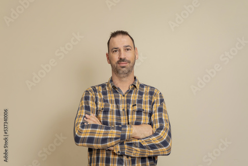 Cheerful confident Caucasian man in checkered shirt with arms crossed on his chest, isolated on beige background. Modern businessman in meeting, online education and presentation, video call.