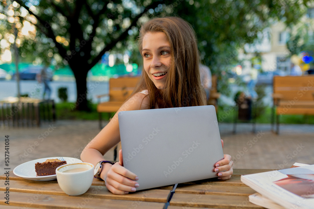 lovely cute lady with long hair sitting on street cafeteria with laptop and having coffee break inn warm sunny day. People sincere emotions lifestyle concept.
