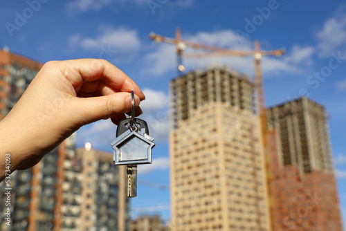 Real estate agent, keychain in shape of a house and key in female hand on background of construction cranes and new buildings. Byung apartment or renting property
