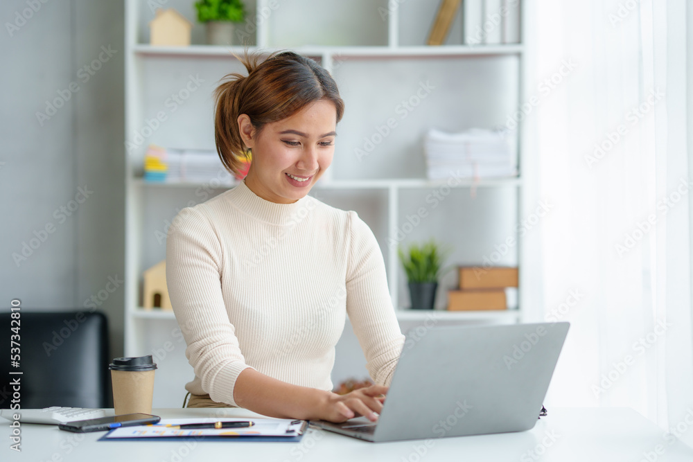 Portrait of smiling Asian businesswoman enjoying her work on her laptop at the office.