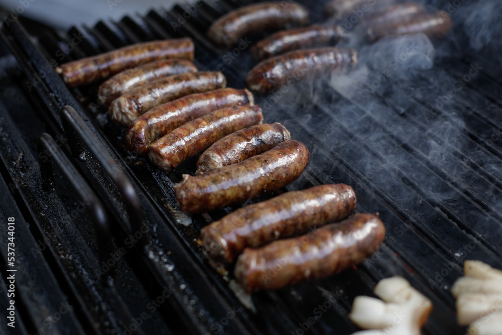 Shallow depth of field (selective focus) details with pork sausages cooking on a barbecue grill, in a European farmers market.
