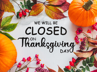 We will be closed for the Holidays. Beautiful Thanksgiving sign. Bright pumpkins, tree leaves, red berries and colorful flowers lying on an empty table. Close-up, top view. Holiday concept