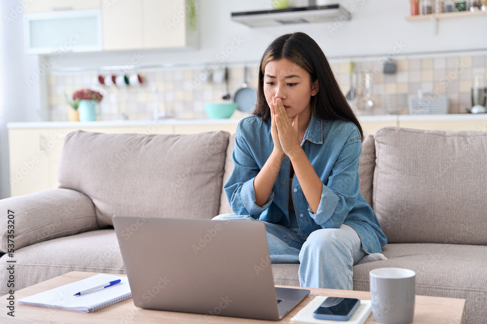 Nervous asian woman looking at laptop screen worrying about bad news Nervous asian woman looking at laptop screen worrying about bad news