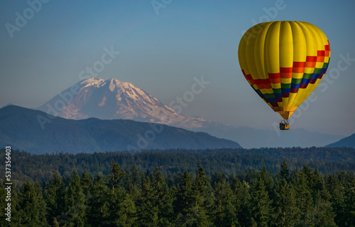 Bird's Eye View of a Hot Air Balloon Floating Over a Forest with Mount Rainer in the Background.