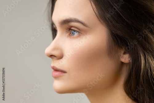 Side view beauty portrait of beautiful woman with perfect skin, looking away with thoughtful expression, wearing casual style jacket. Indoor studio shot isolated on gray background.