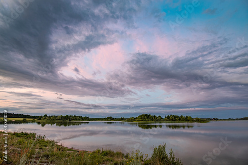 Evening rural landscape with a pond and clouds. Dramatic sky over the horizon.