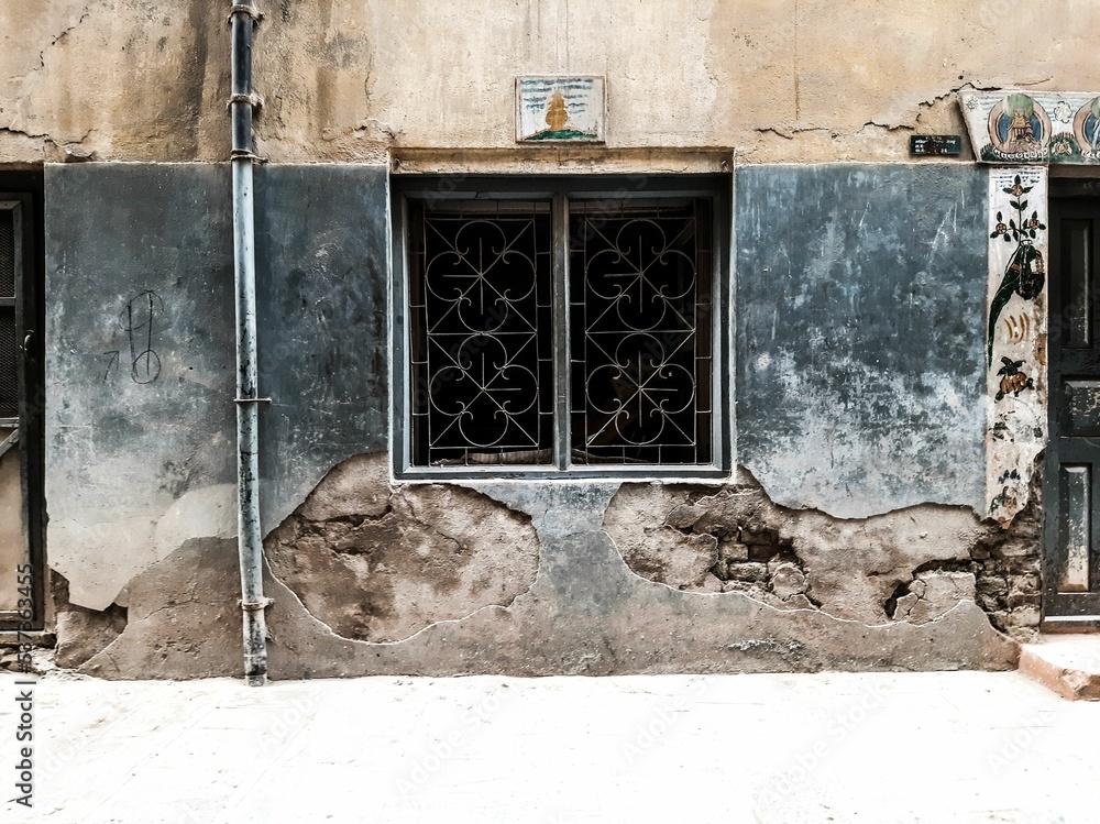 Closeup of the small square window of an old building with its walls deteriorating - obrazy, fototapety, plakaty 
