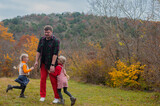 dad has fun playing catch-up with his little twin daughters in an autumn meadow on a warm day
