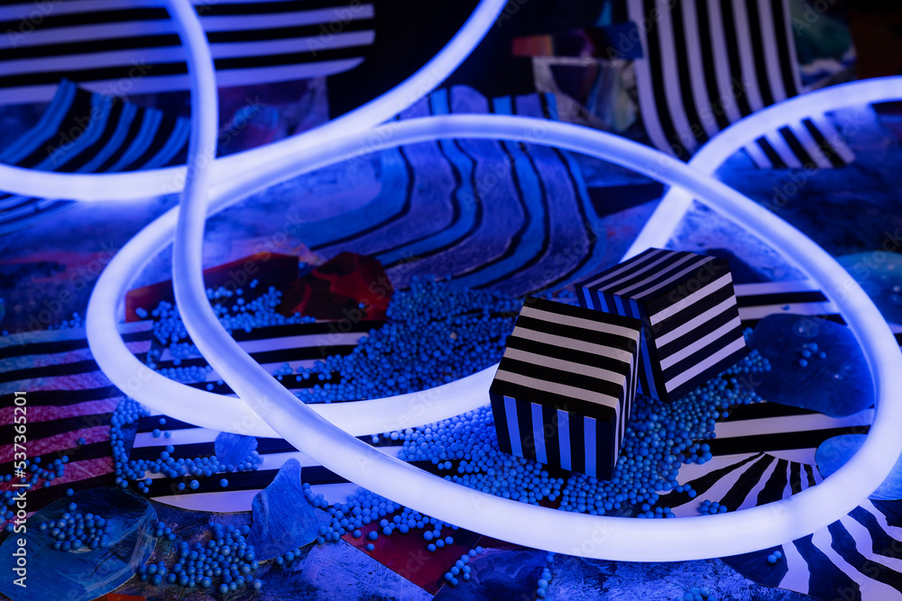 Striped cubes and flexible blue neon light on abstract collage background Striped cubes and flexible blue neon light on abstract collage background