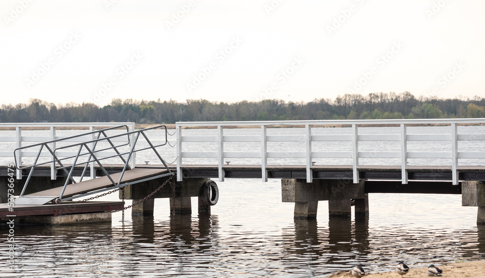 A white wooden pier over the water. Wooden structure on the beach by the lake.