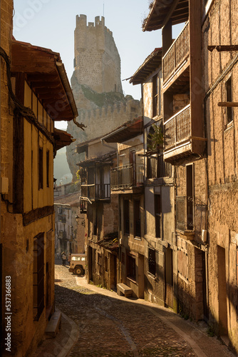 Cityscape with old, stone buildings in a street of the picturesque medieval town of Frias with the tower of the castle in the background, Burgos, Spain