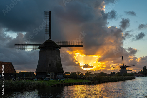 Dramatic sunset sky with silhouettes of historical dutch windmills along the canal in the city of Alkmaar