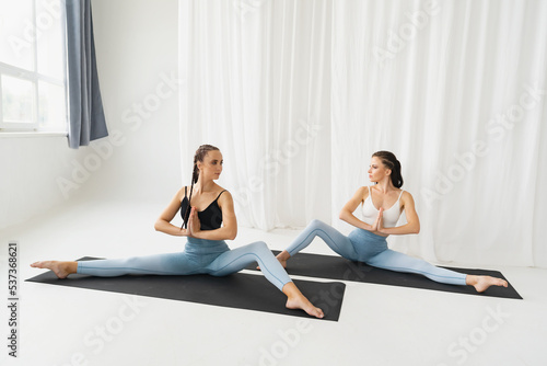 Two beautiful young girls are doing yoga in a snow-white room