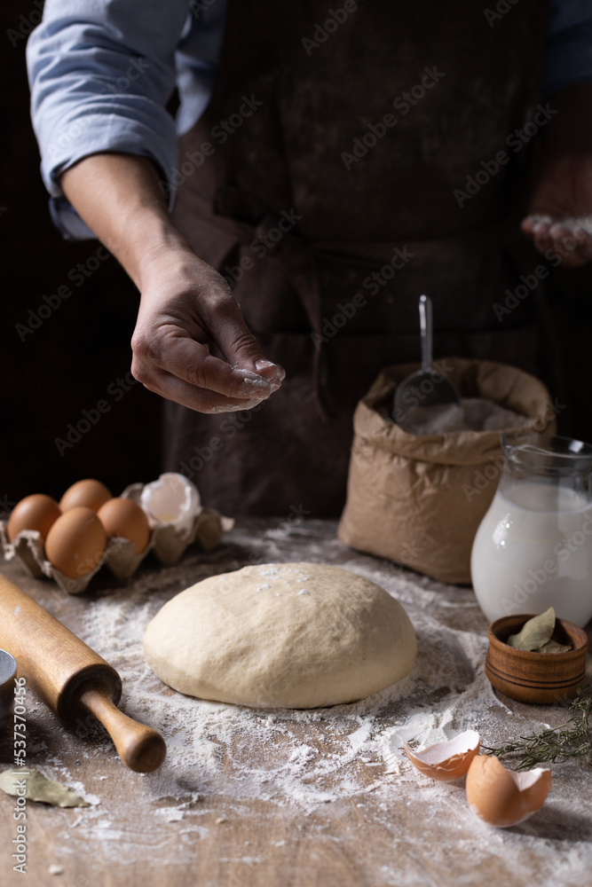 Obraz premium Baker chef man sprinkling flour at dough bread and bakery ingredients for homemade cooking on table