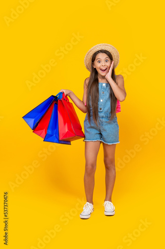 amazed teen kid with shopping bags on yellow background. full length
