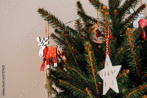 Christmas tree with different wooden decorations. Christmas garland and Christmas lights. White and red colors. Christmas deer, star, snowflake, Bullfinch (ID: 537371429)