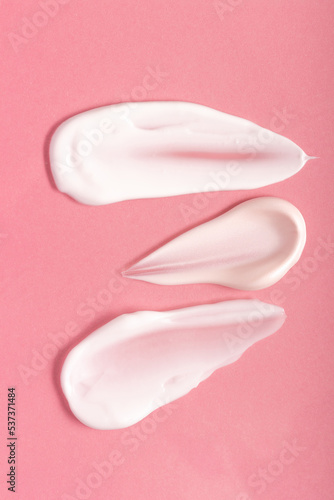 Texture of smears of cream and serum on a pink background. Cosmetics smeared on the table.