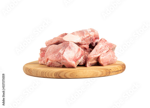 Pieces of raw fresh pork stew on a round cutting board over white background.