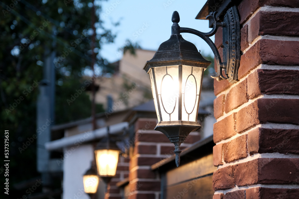 The dark street is illuminated by street lamps. Vintage lantern on a brick wall in the evening