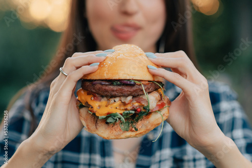 Young attractive hungry woman bites a big hamburger outdoor. Close up.