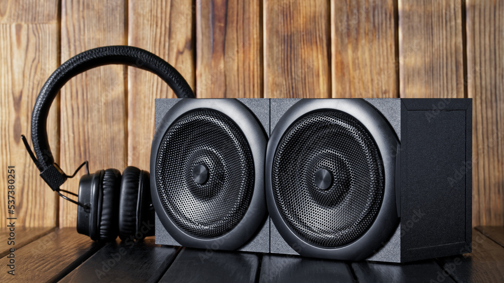 Two wooden audio speakers with metal grill and wireless headphones