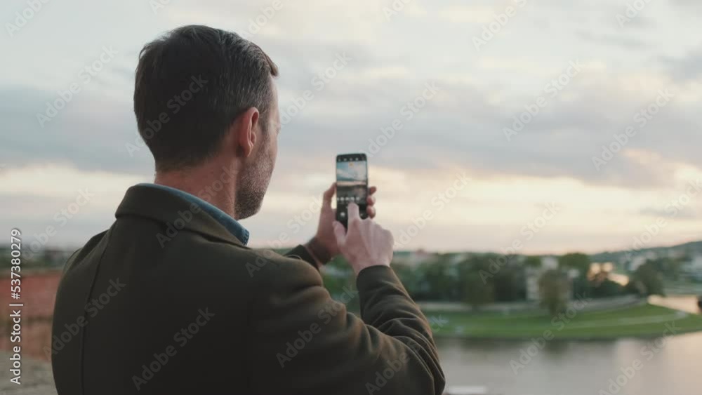 Man takes video of the picturesque river bank. Back view Man takes video of the picturesque river bank. Back view