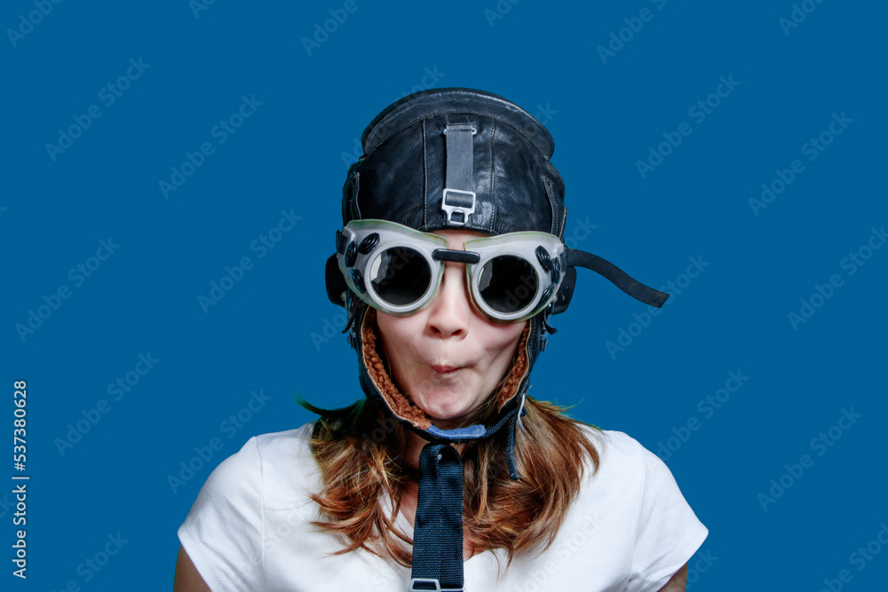 Girl in an aviator helmet, portrait on a blue background. A young girl-pilot against the sky. A symbol of travel and development - a teenager dreams of flying Girl in an aviator helmet, portrait on a blue background. A young girl-pilot against the sky. A symbol of travel and development - a teenager dreams of flying