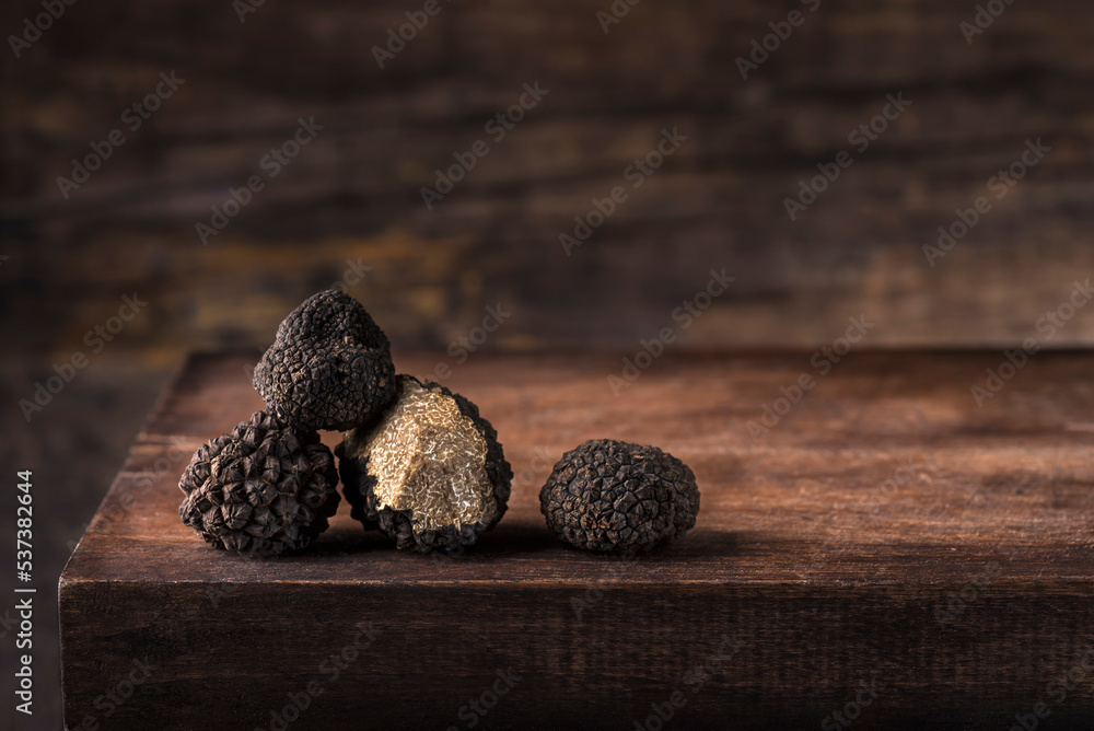 Black truffles in antique  wooden board, rustic style, low key, selective focus, macro, copy space for text. Season of black truffle. Autumn gourmet cuisine of Piedmont,  Italy, Spain and France - obrazy, fototapety, plakaty 