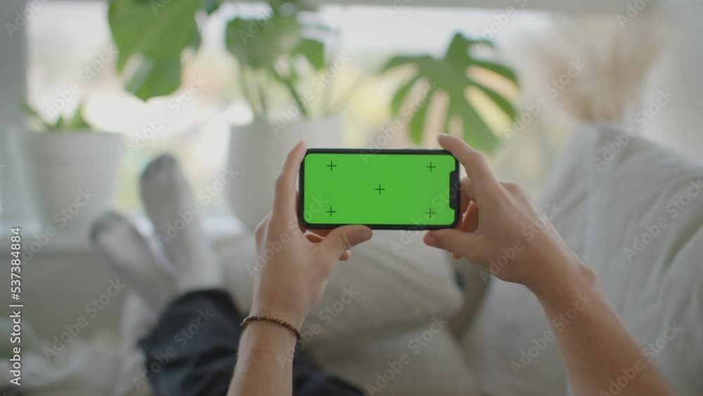 Man relaxing on couch interacting with phone, landscape, green screen mockup