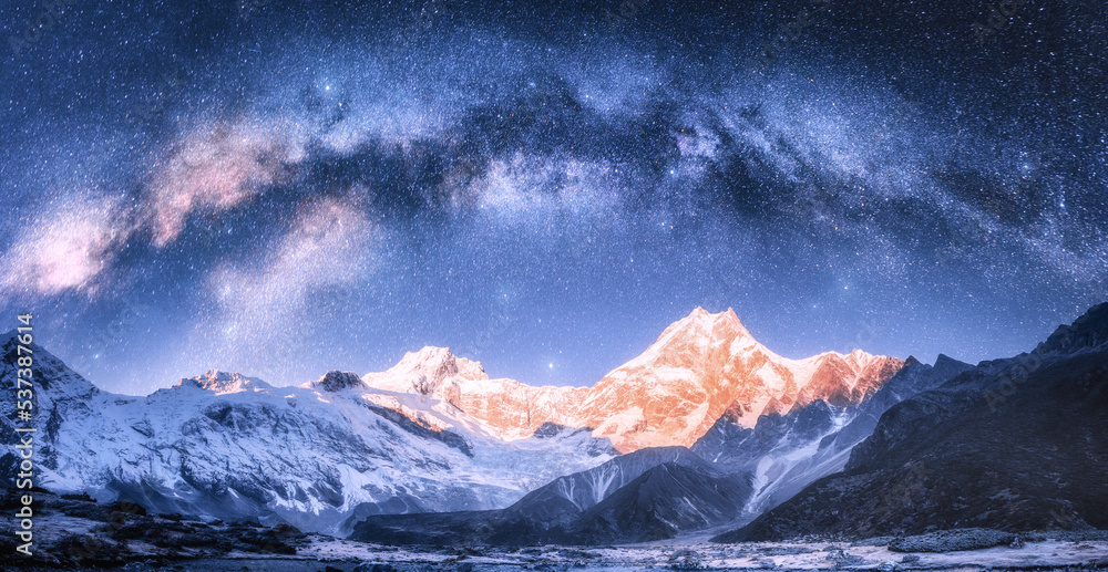 Milky Way arch over snowy mountains at starry night in winter. Landscape with snow covered high rocks, blue sky with stars in Nepal. Bright arched milky way in Himalayas. Space background. Nature