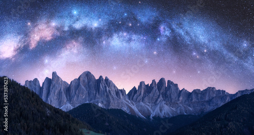 Acrhed Milky Way over beautifull rocks at starry night in summer in Dolomites  Italy. Purple sky with stars and bright milky way arch over high alpine rocky mountains. Space background. Nature