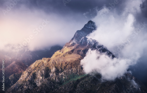 Mountain peak in low clouds at colorful sunset in Nepal. Dramatic landscape with beautiful high rocks in fog, moody sky, sunlight, tress, grass at sunset. Nature. Himalayan mountains. Scenery © den-belitsky