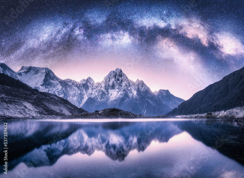 Milky Way arch over snowy mountains and lake at night. Landscape with snow covered high rocks  violet starry sky  reflection in water in Nepal. Sky with stars. Bright milky way in Himalayas. Space
